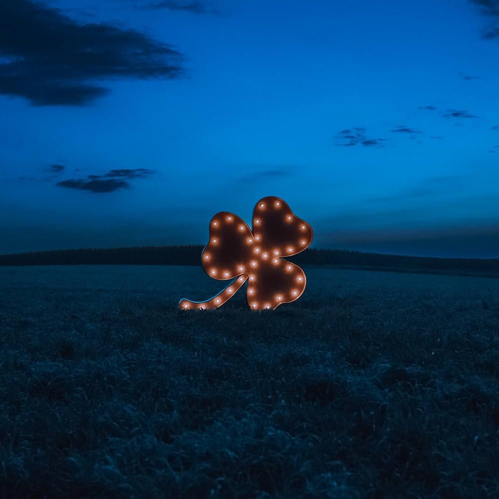 The cover of Grayscale's "The Hart" depicting a sculpture of a four-leaf clover with light bulbs around the edges, standing in a field at night under a blue sky