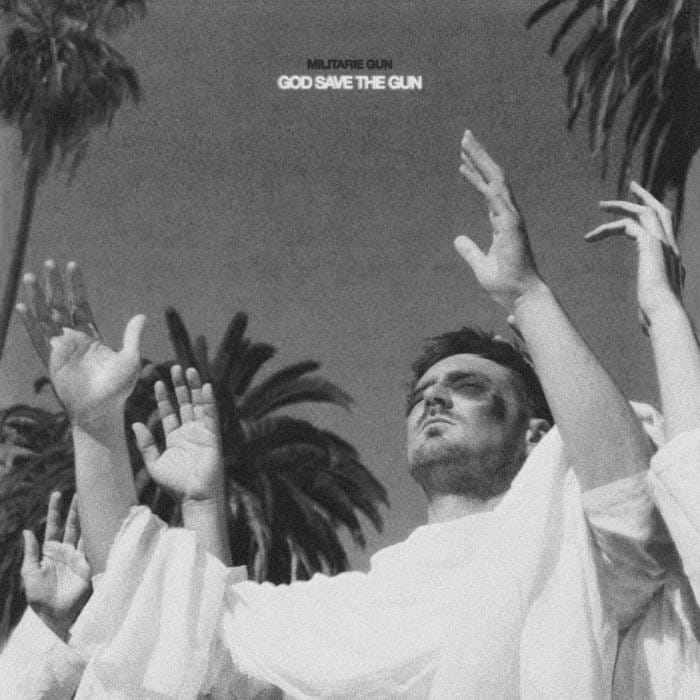 The cover of Militarie Gun's "God Save The Gun" depicting a cult-like image of people in white robes, eyes closed and hands raised, as if in prayer. The only one whose face we can see is a man with a bruised face.