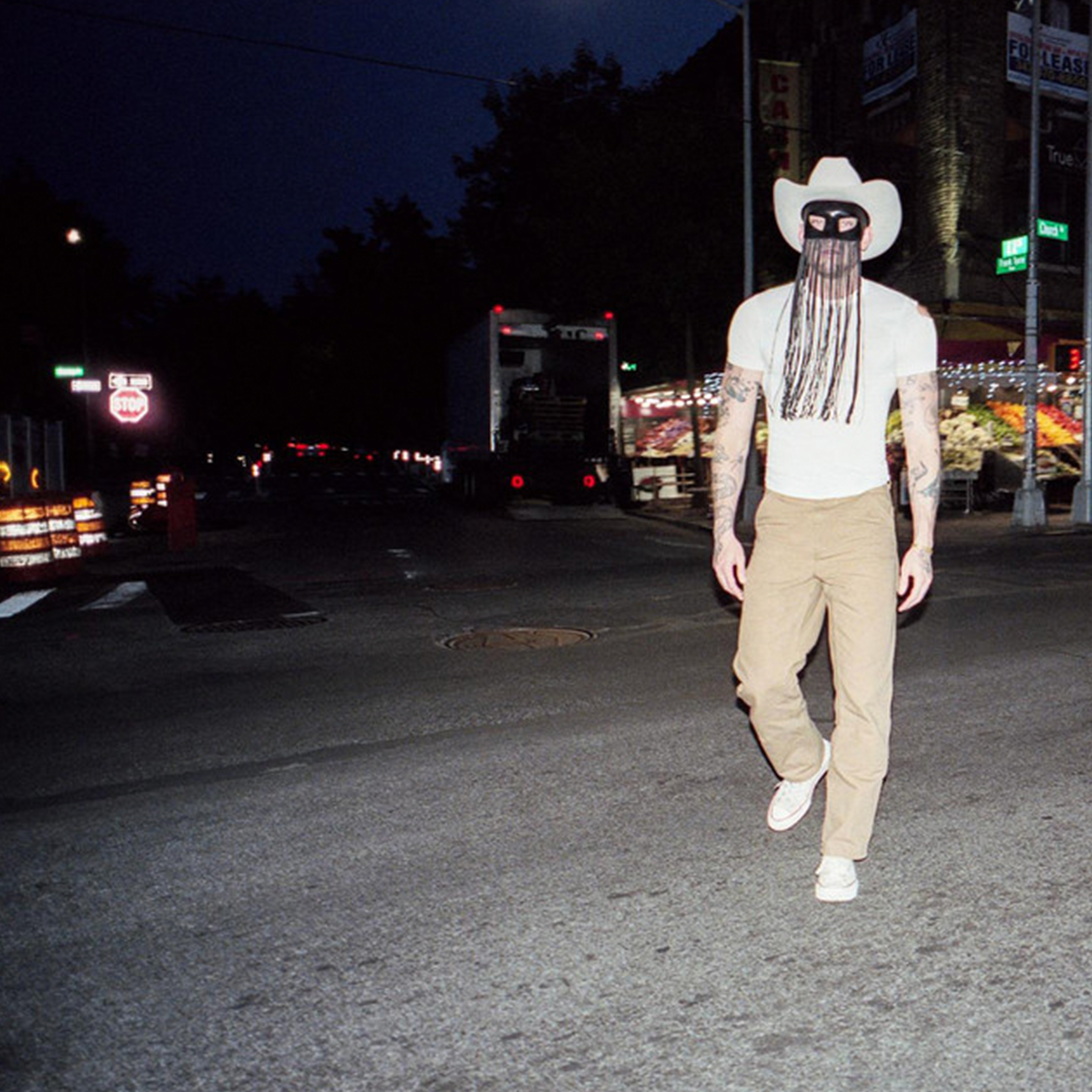 The cover of Orville Peck's "Appaloosa" depicting the singer in his trademark half-mask and a cowboy hat standing in a city street at night